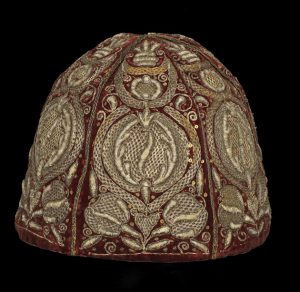 COSTUME cap; nightcap circa 1640-1660 overall: 180 mm Man’s night cap made from red silk velvet cut in six conical sections embroidered in metal threads with pomegranates and embellished with spangles. Said to have belonged to Major Buntine.